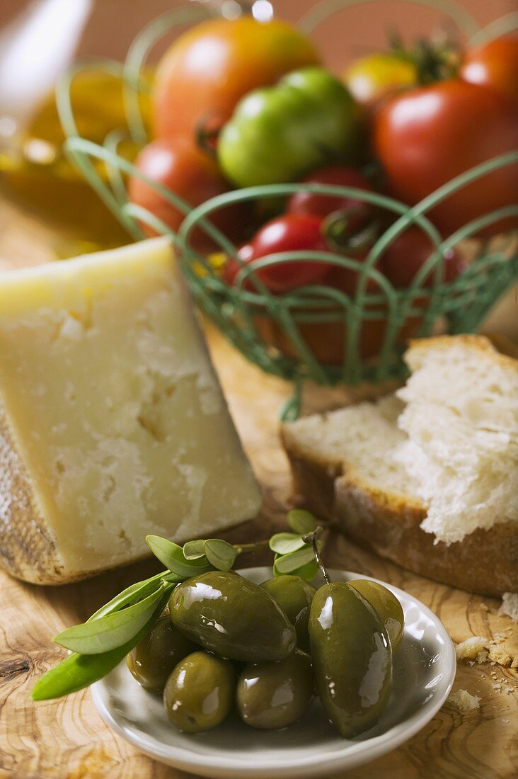 Tomaten im Drahtkorb, Oliven, Käse, Brot und Olivenöl