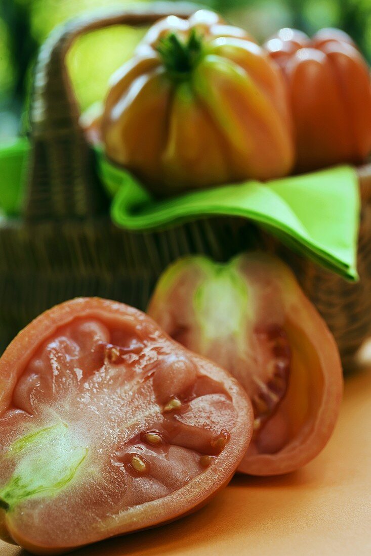 Zwei Tomatenhälften, dahinter Tomaten im Korb