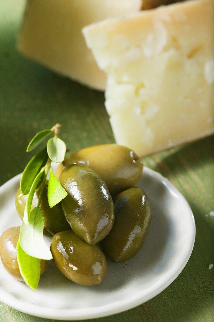Green olives with olive sprig on plate, cheese in background
