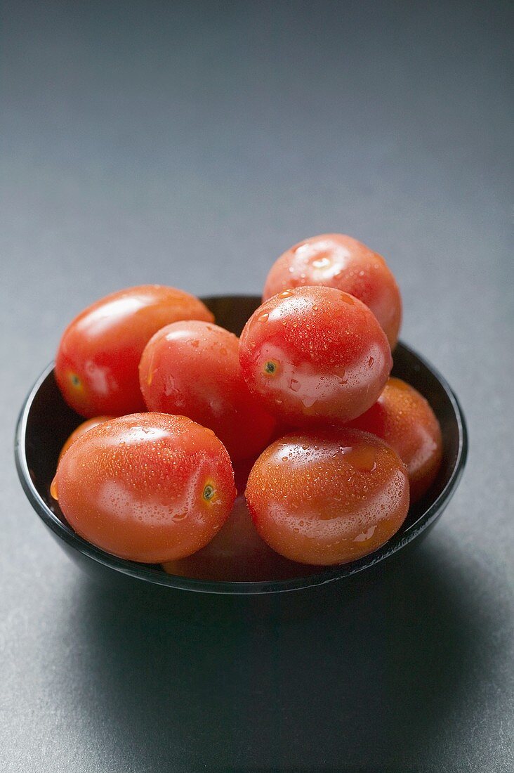 Cherry tomatoes with drops of water in black bowl