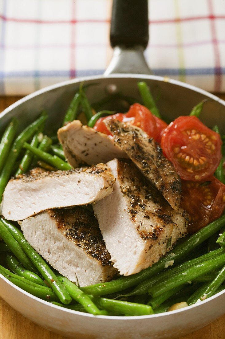 Chicken breast with green beans and tomatoes in frying pan