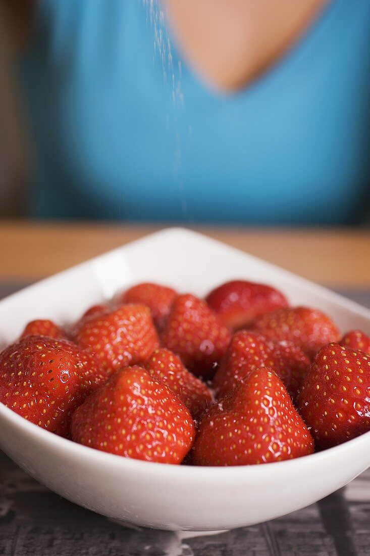 Strawberries in white bowl, woman in background