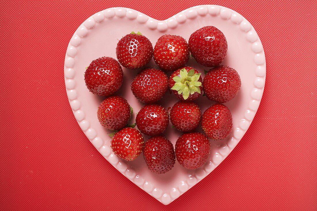 Strawberries on pink heart-shaped plate (overhead view)
