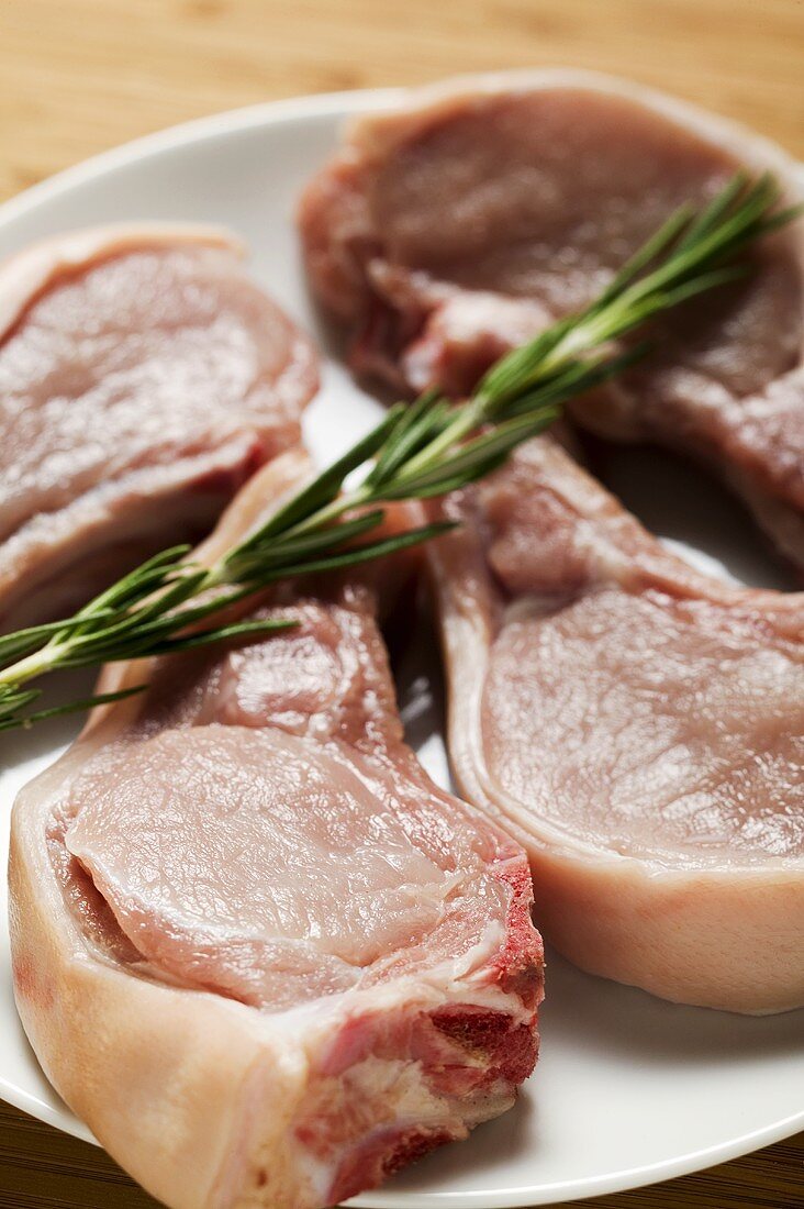 Raw pork chops with rosemary on plate