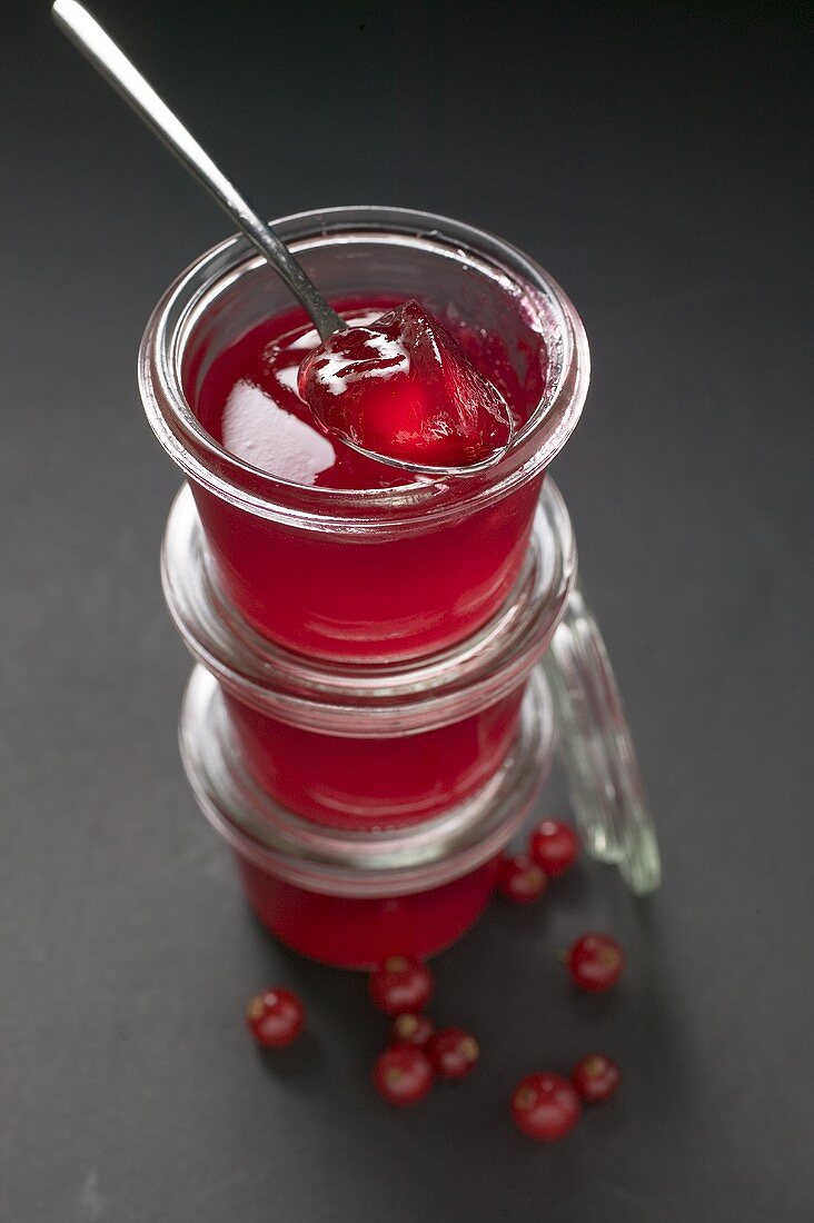 Three jars of redcurrant jelly, one opened, with spoon