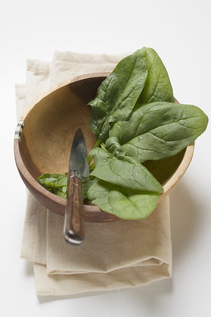 Several spinach leaves in wooden bowl with knife