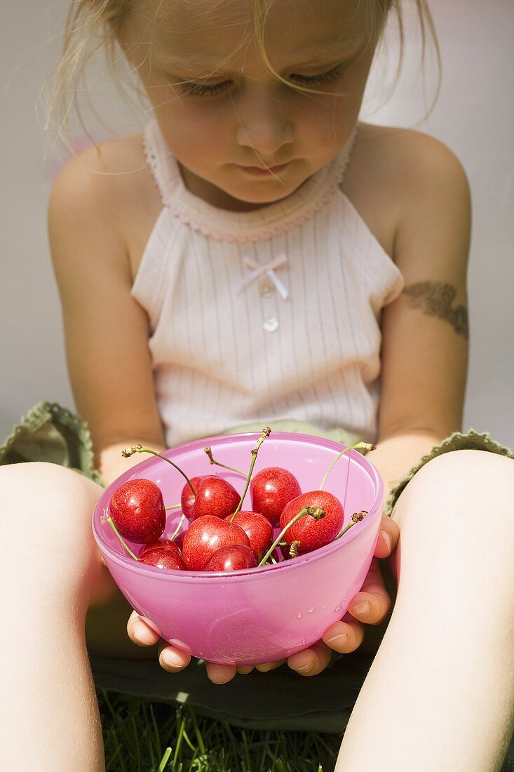 Seated girl holding bowl of fresh red cherries