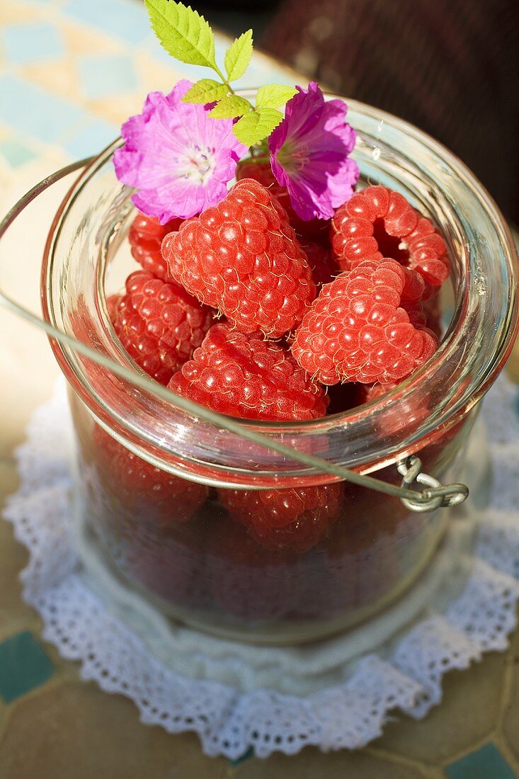 Fresh raspberries and purple flowers in preserving jar