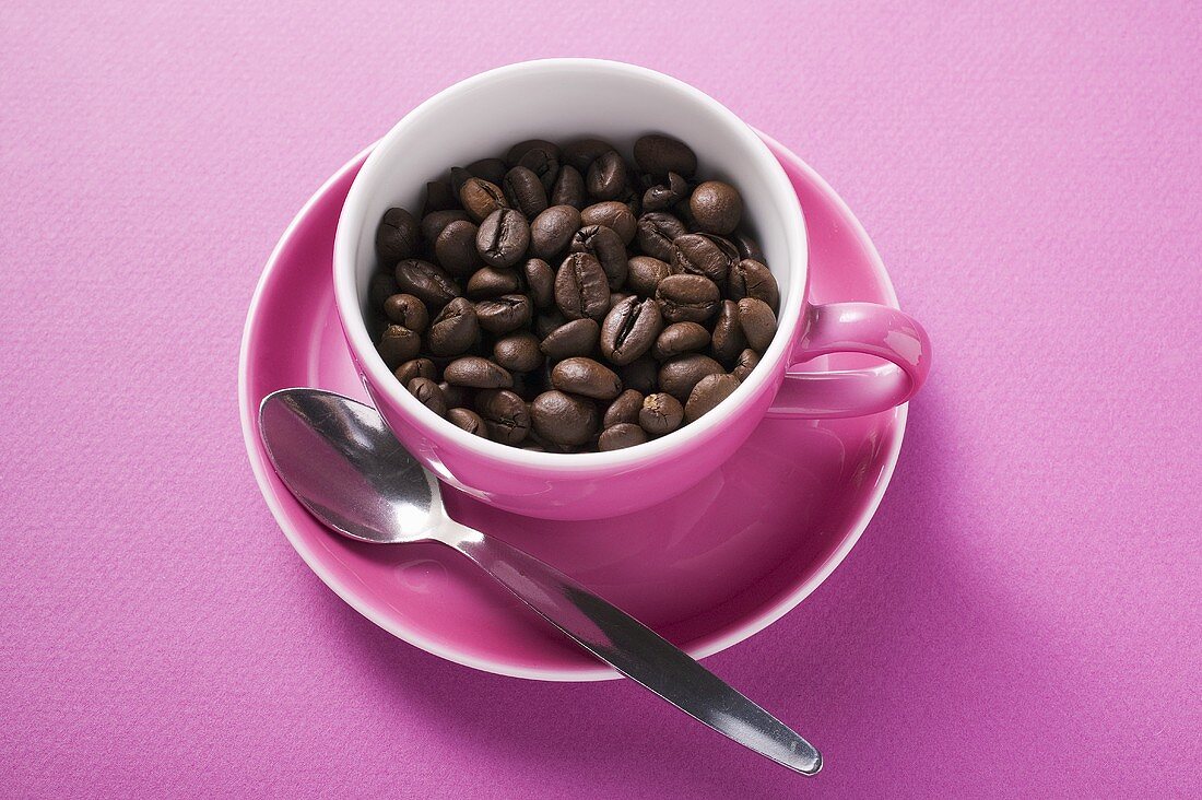 Coffee beans in pink coffee cup with spoon in saucer