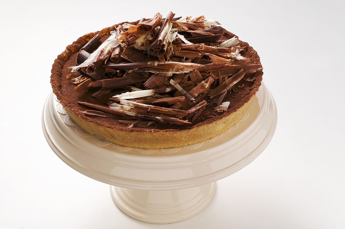 Whole chocolate tart with chocolate curls on cake stand