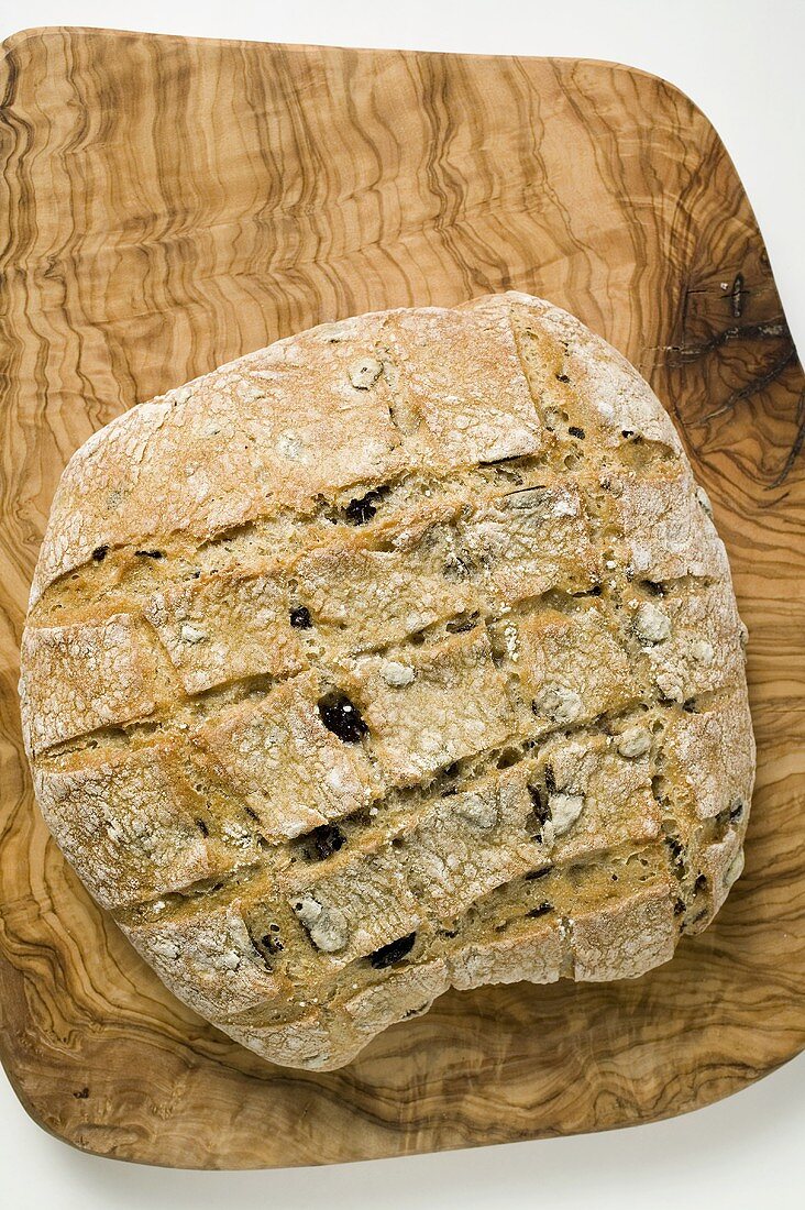 Crusty olive bread on chopping board (overhead view)