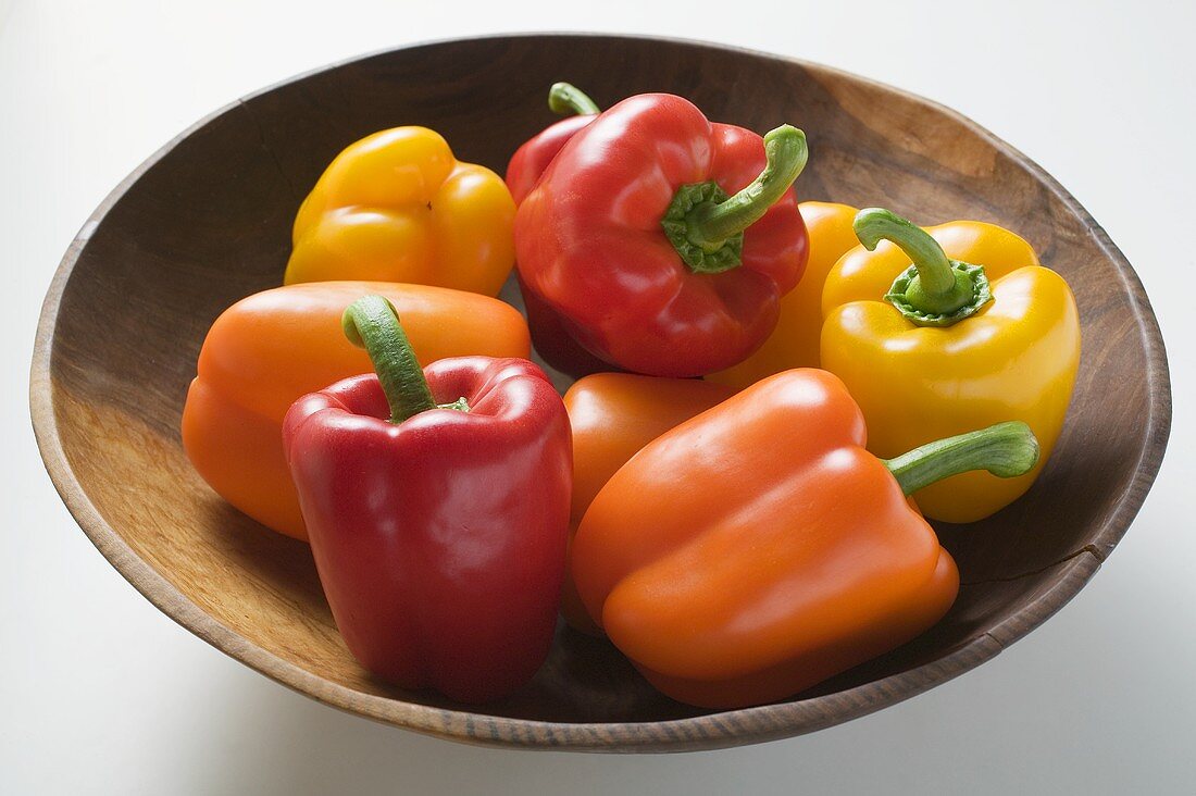 Yellow, orange and red peppers in wooden bowl