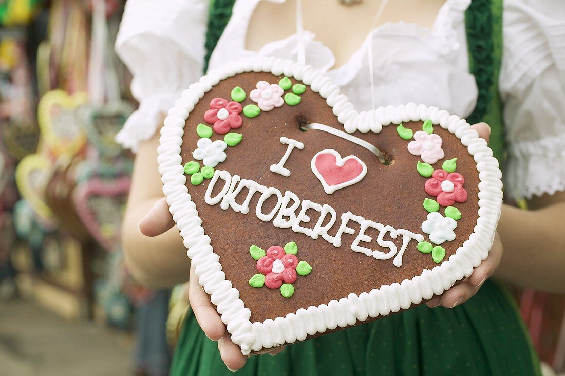 Frau in Tracht hält Lebkuchenherz beim Oktoberfest