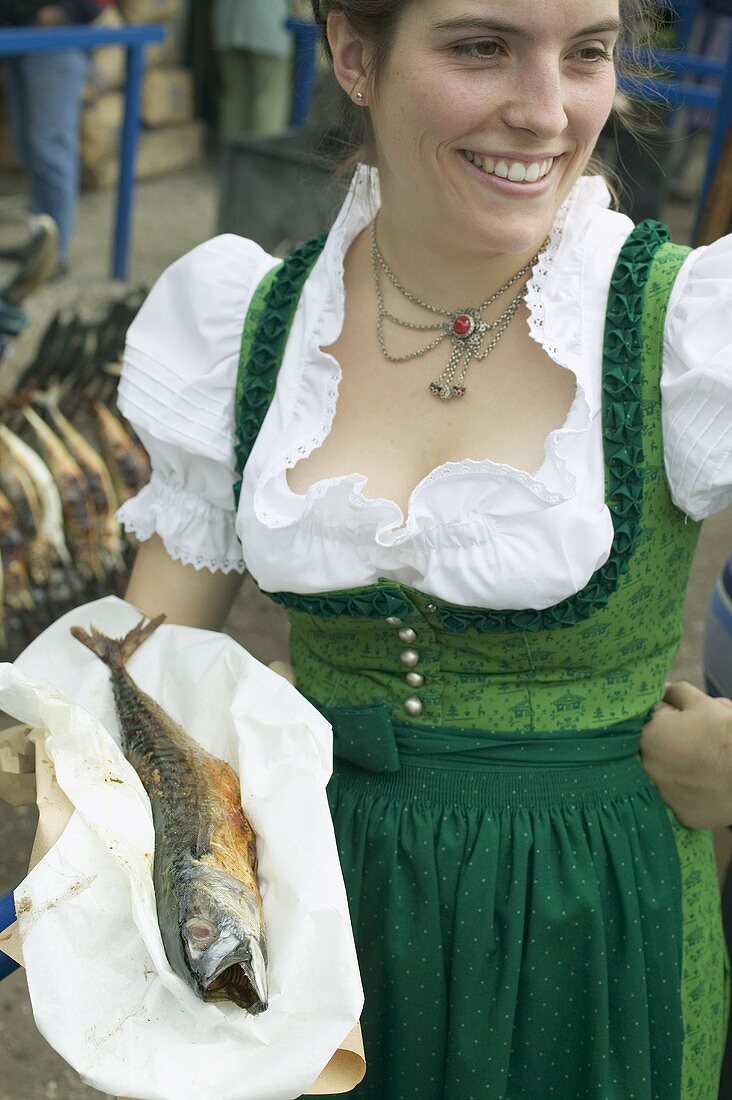 Frau in Tracht hält Steckerlfisch beim Oktoberfest