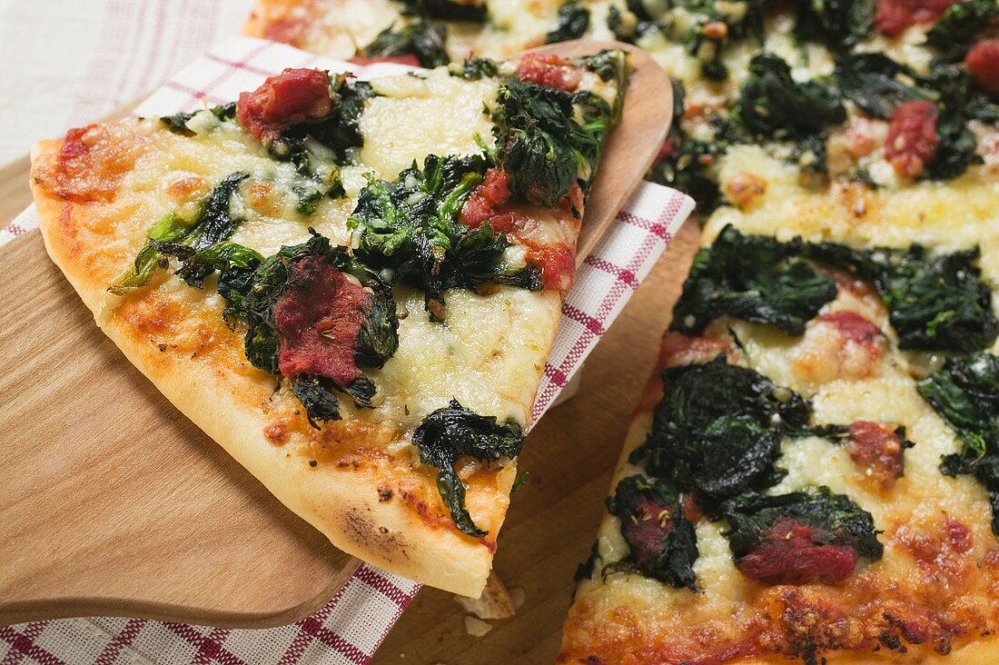 Spinach, tomato and cheese pizza with slice on server