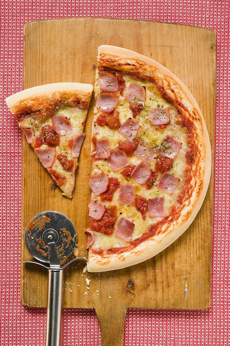 Ham pizza on chopping board (half and a slice)