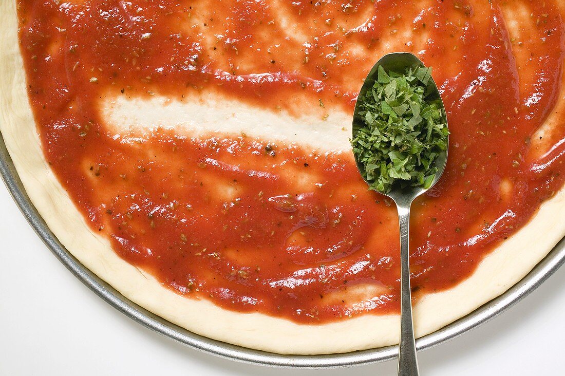 Pizzateig mit Tomatensauce und Löffel Oregano (Close Up)