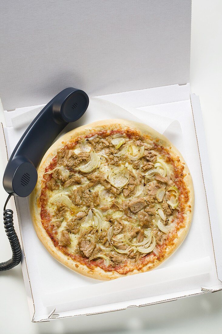 Thunfisch-Zwiebel-Pizza im Pizzakarton mit Telefonhörer