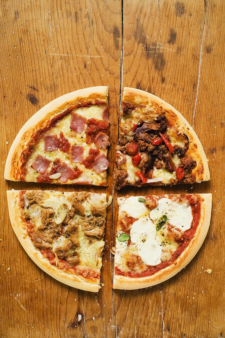 Pieces of four different pizzas on wooden background