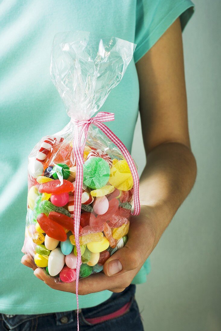Hand holding cellophane bag of coloured sweets