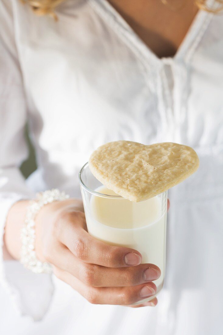 Hand hält Glas Milch mit einem Plätzchen