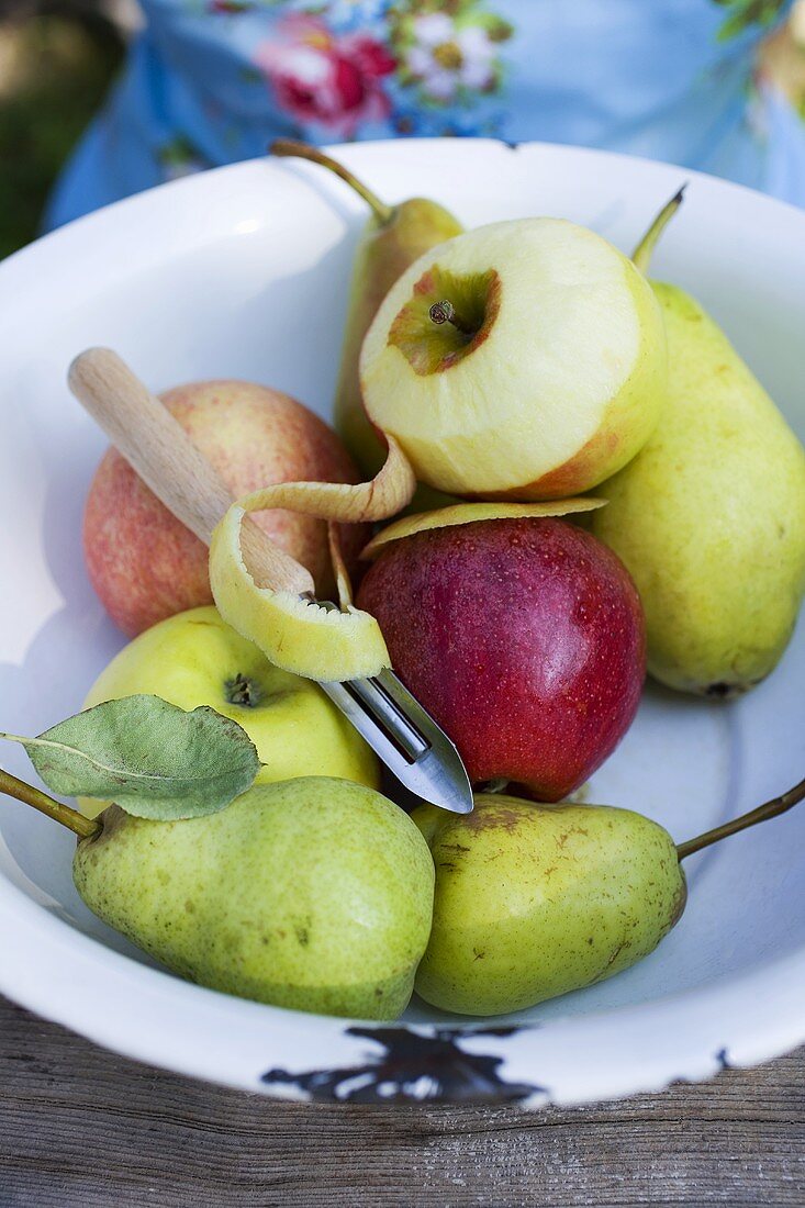 Äpfel, einer halb geschält, und Birnen in Schüssel