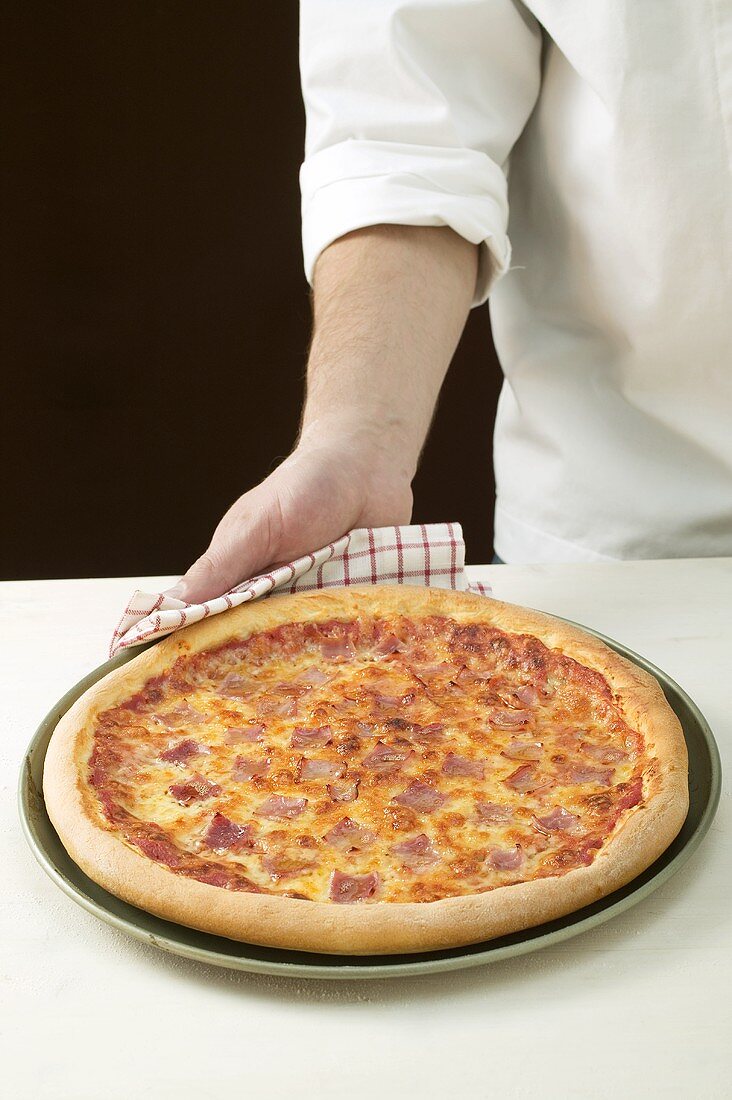 Chef serving American-style ham pizza