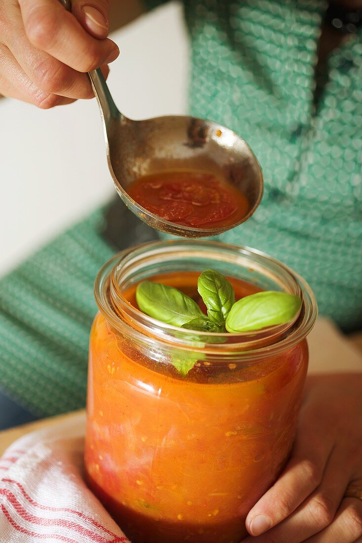 Frau hält Einmachglas und Kelle mit Tomatensauce