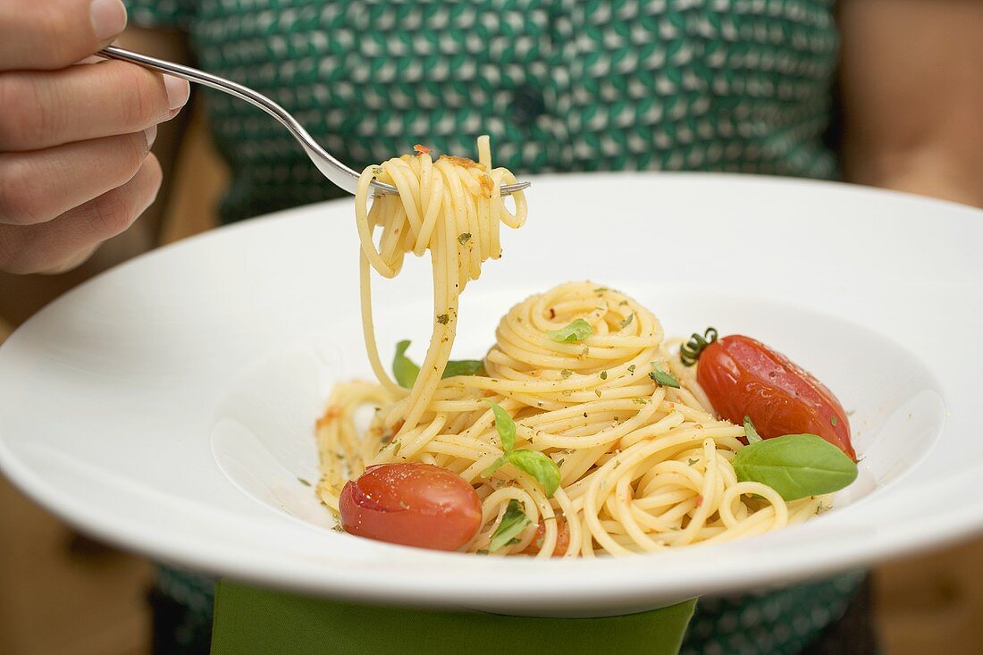 Woman holding plate of spaghetti with tomatoes and basil