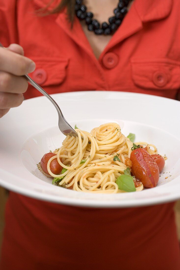 Frau isst Spaghetti mit Tomaten und Basilikum