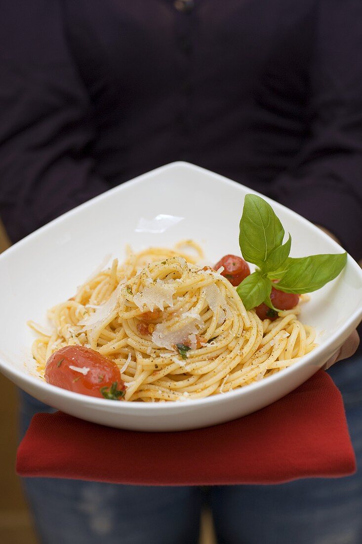 Person holding plate of spaghetti with Parmesan and basil