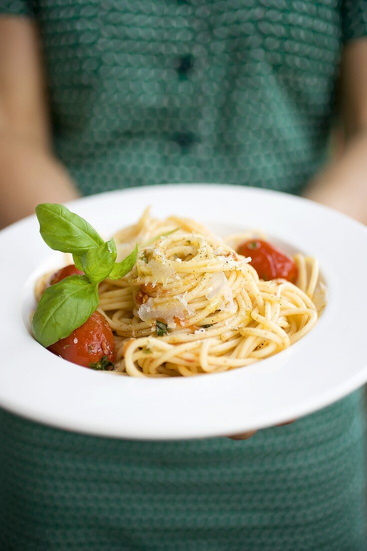 Woman holding plate of spaghetti with Parmesan and basil