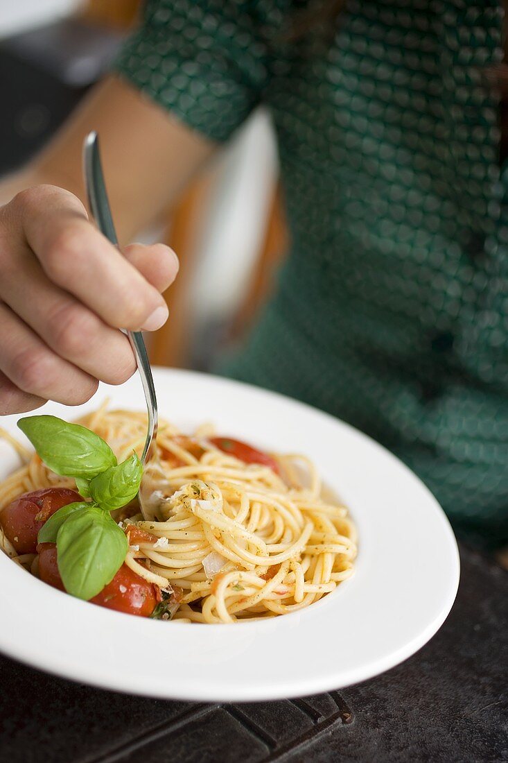 Frau isst Spaghetti mit Tomaten, Parmesan und Basilikum