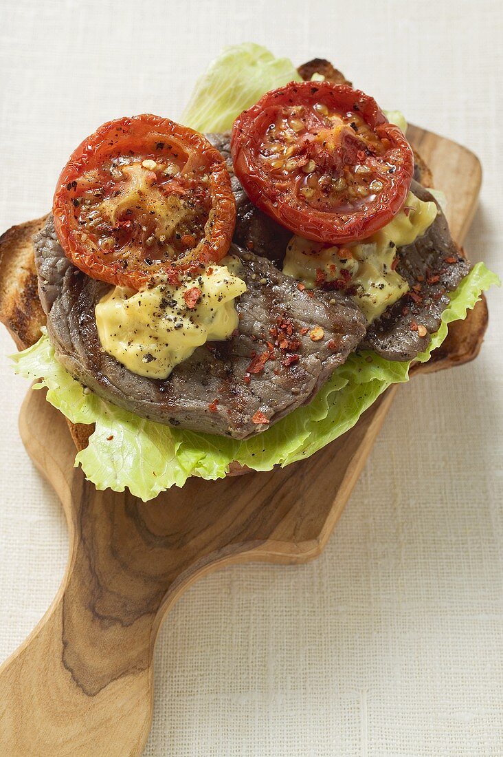 Beef steak and tomatoes on toast on chopping board