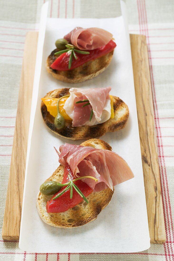 Several crostini with raw ham, peppers and giant capers