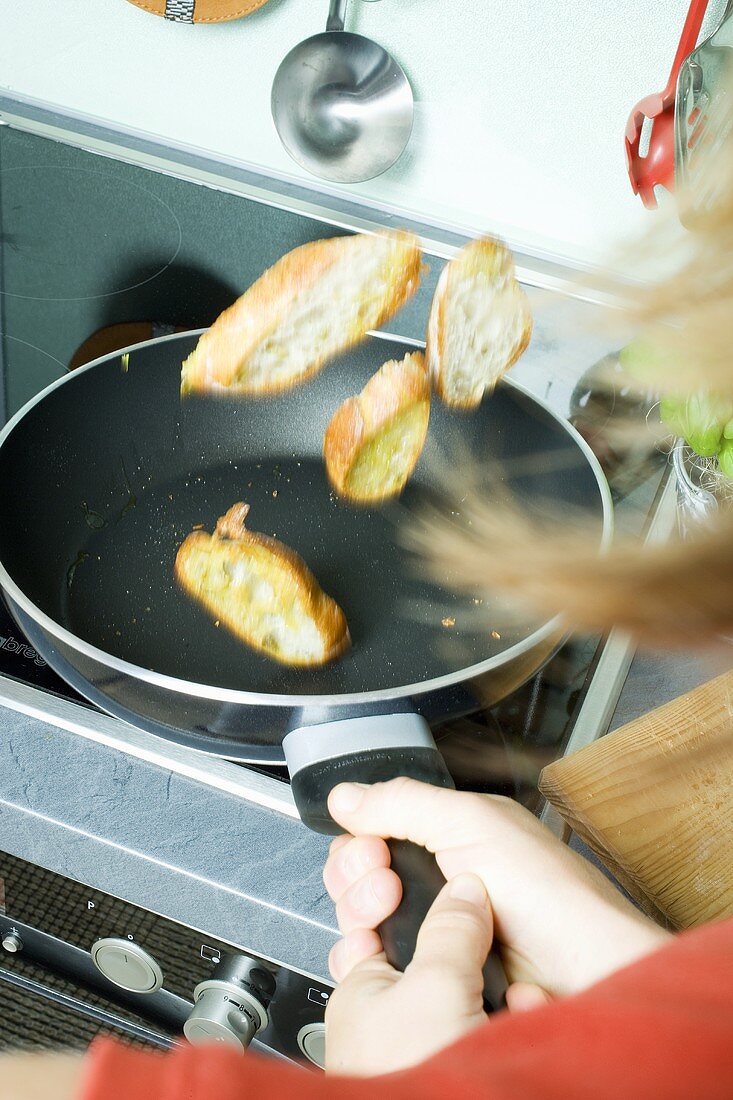 Geröstete Baguettescheiben in Pfanne hochwerfen