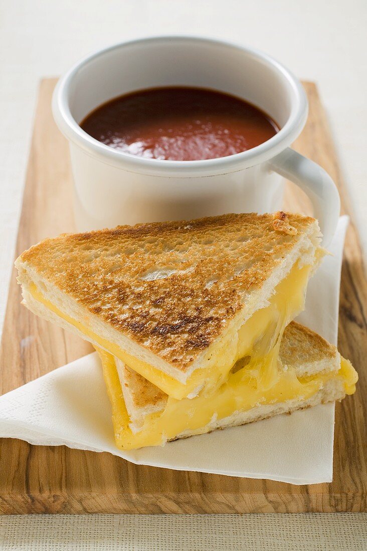 Käsetoasts und eine Tasse Tomatensuppe auf Schneidebrett