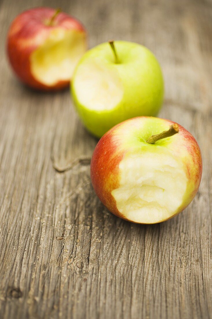 Three apples with bites taken on wooden background