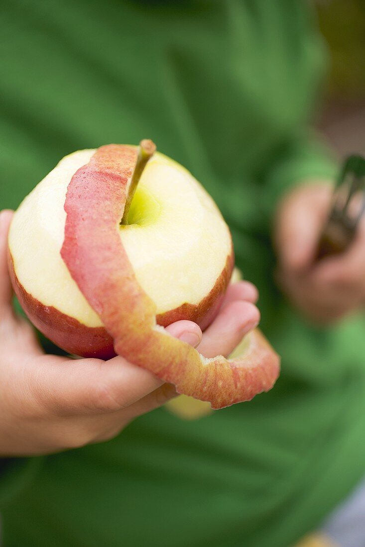 Kinderhände halten halb geschälten roten Apfel