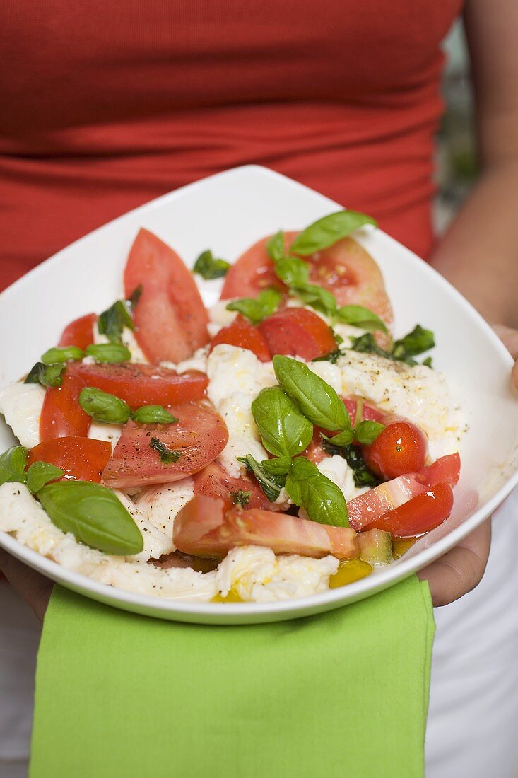Woman holding bowl of tomatoes with mozzarella and basil
