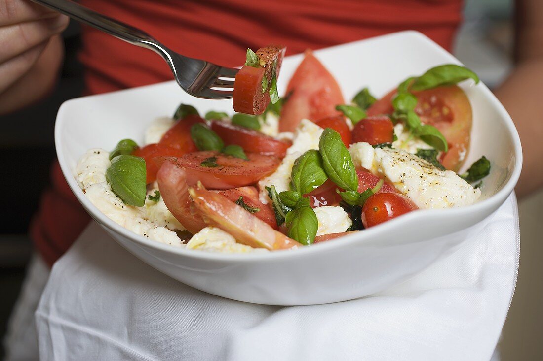 Frau isst Tomaten mit Mozzarella und Basilikum