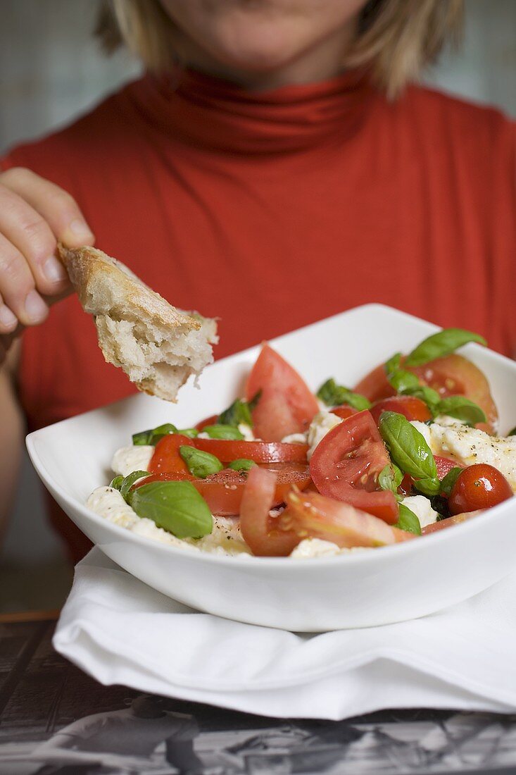 Frau isst Brot zu Tomaten mit Mozzarella und Basilikum