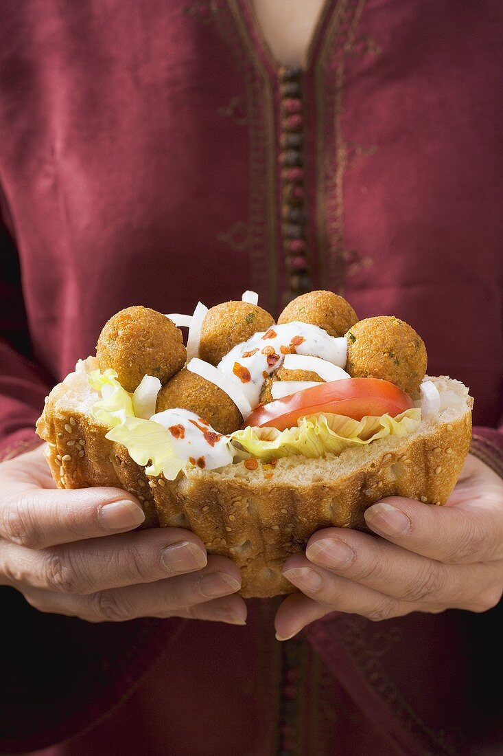 Woman holding flatbread filled with falafel (chick-pea balls)