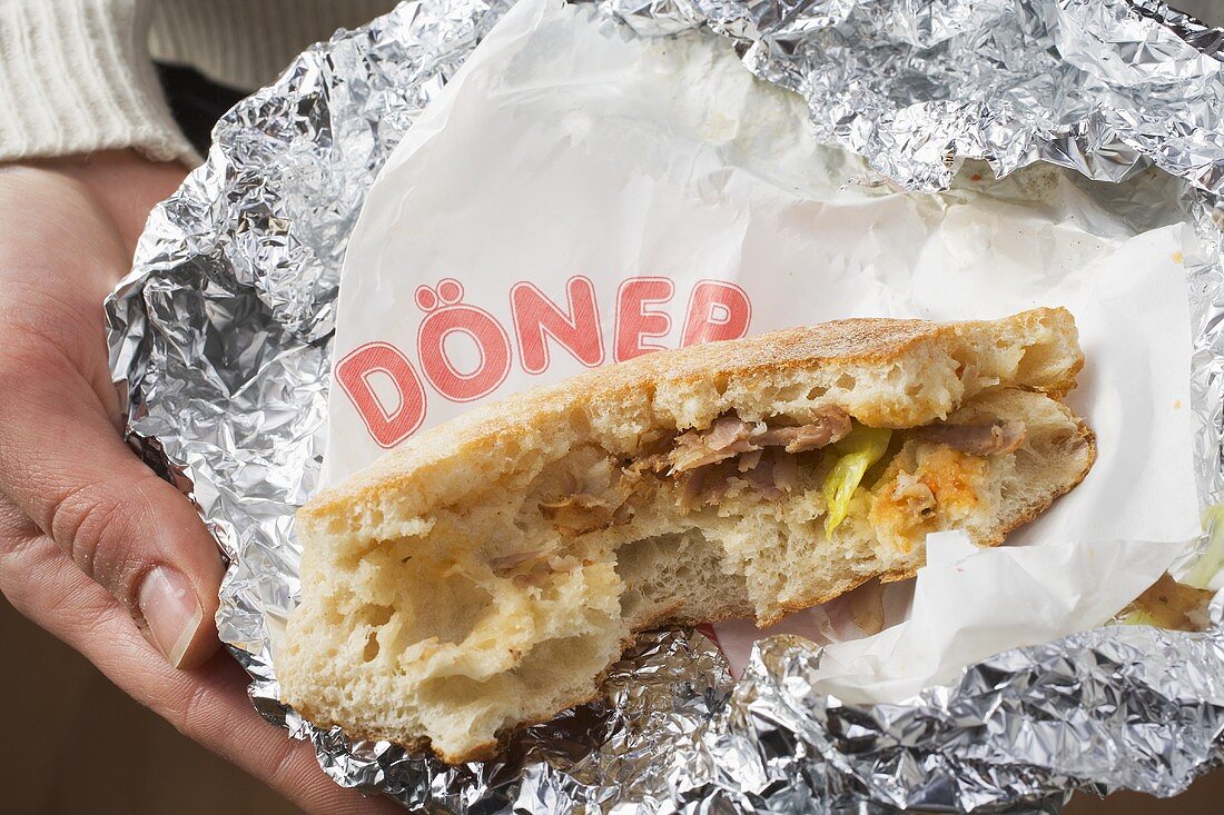 Person holding döner kebab, partly eaten, in aluminium foil