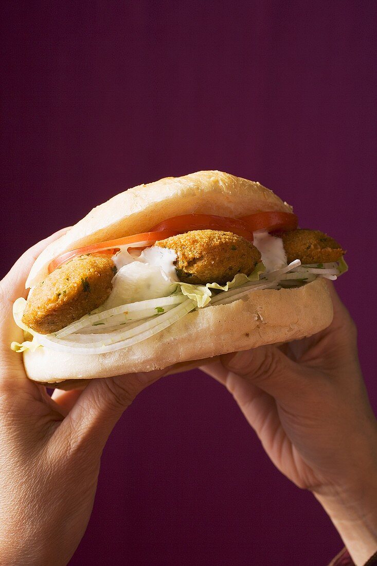 Hands holding flatbread filled with falafel (chick-pea balls)