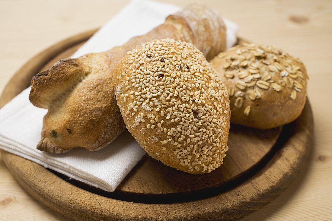 Baguette und Vollwertbrötchen auf Holzteller mit Messer