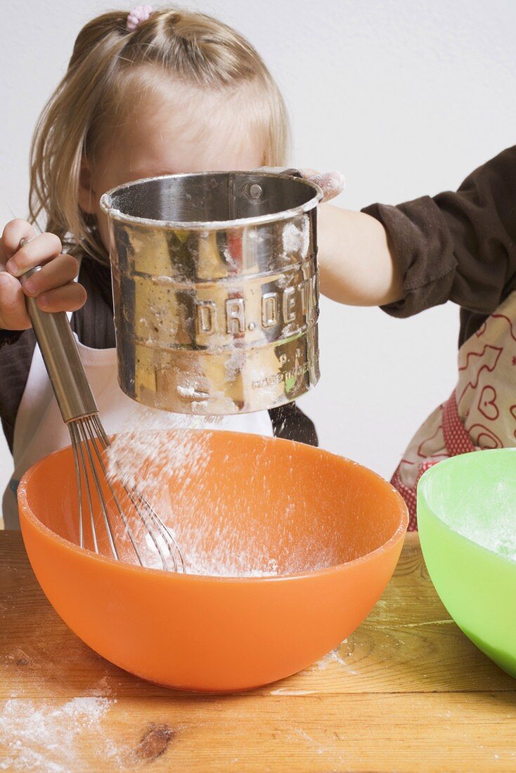 Two children baking (sieving flour into bowl)