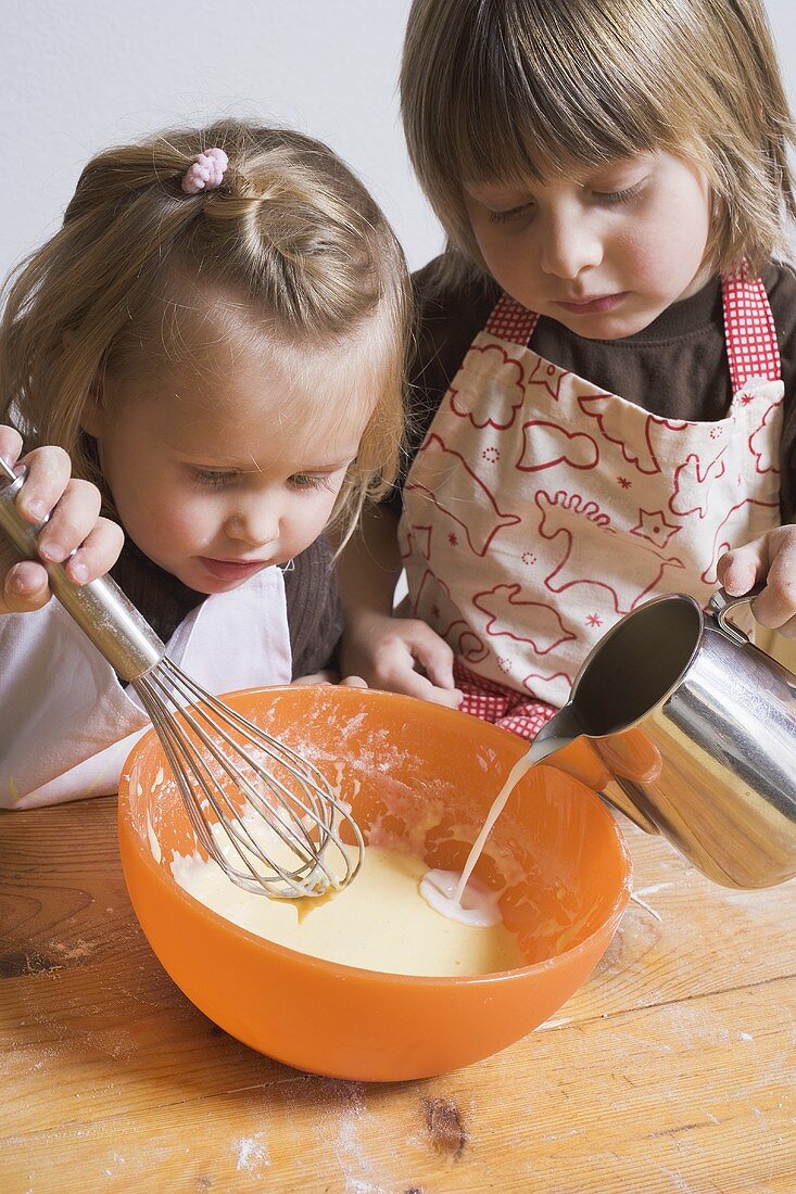 Zwei Kinder bereiten Teig zu (Milch in Schüssel gießen)
