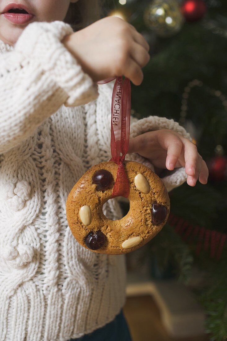 Child holding gingerbread tree ornament in front of Xmas tree