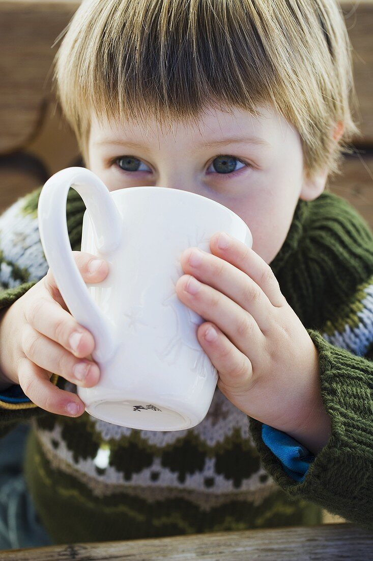 Small boy drinking hot drink in the open air